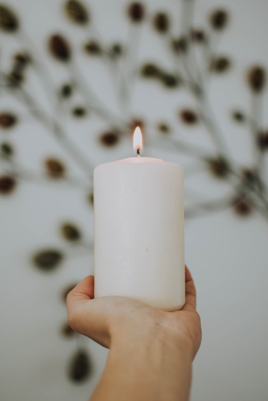 photo of hand holding lit white pillar candle